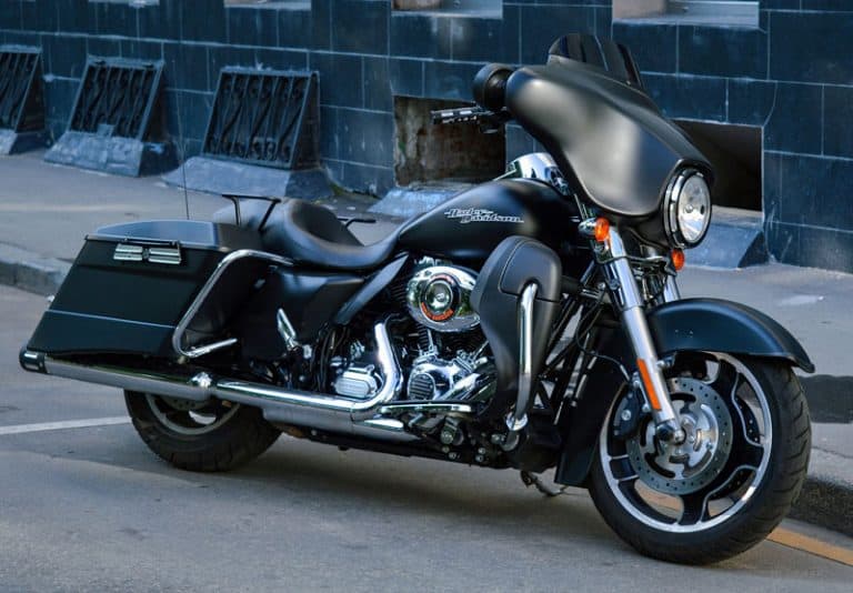 BLACK MOTORCYCLE PARKED ON PAVEMENT AGAINST BRICK WALL