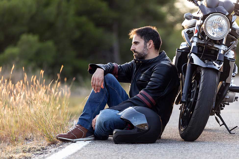 man sitting next to broken down motorcycle